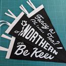 Three black triangular pennant flags with white fringe and white printed text, arranged on a green cutting mat. The pennants read phrases including 'NORTHERN', 'Be Keen', and 'Fancy a chippy tea?'.